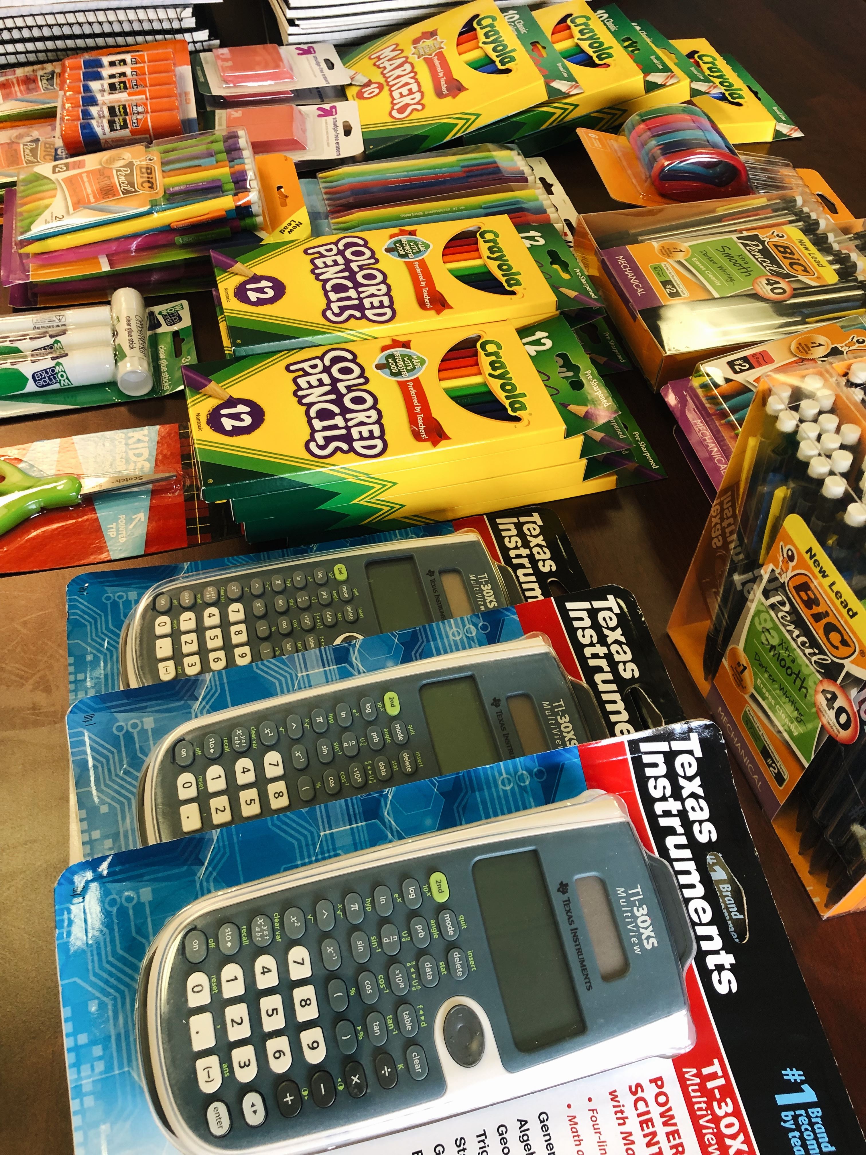 Close up picture of more school supplies: markers, erasers, glue sticks, notebooks, pencils, pens, calculators, etc.